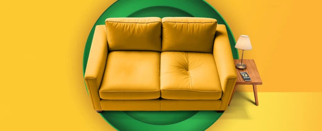 A yellow couch with a dent in it features alongside a coffee table and a smartphone with Joe Fortune Casino’s logo on the screen. On a yellow and gold background.