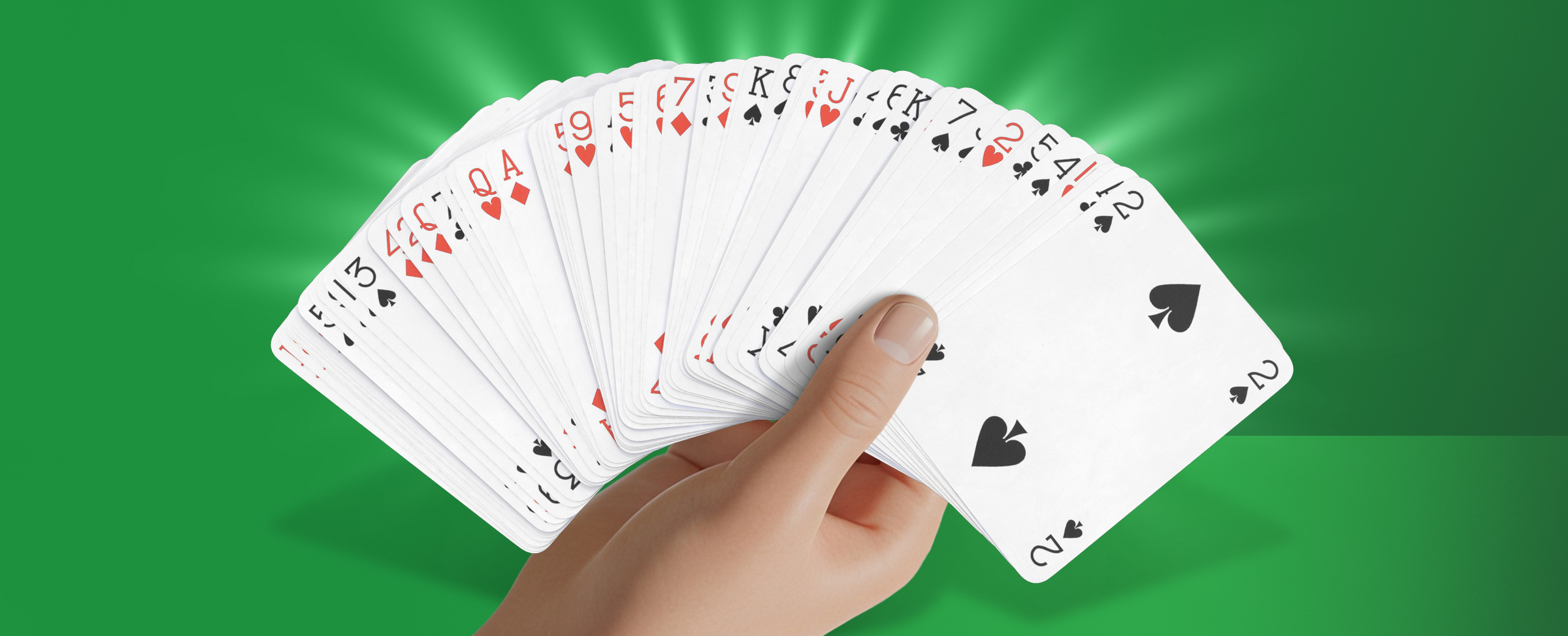 A hand fanning out a full deck of playing cards in a wide arc against a bright green background.