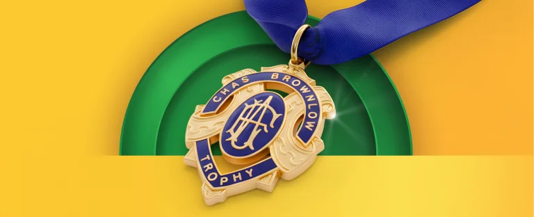 A gold and blue Brownlow Medal featuring the text “Chas Brownlow Trophy” on a blue ribbon, displayed against a bright green and yellow background.