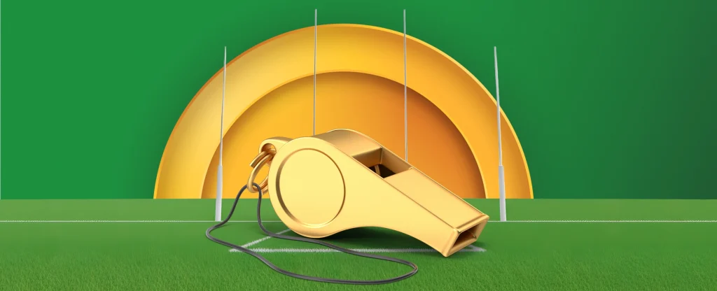 A golden whistle with a black cord resting on an AFL football field with goal posts in the background, with a large golden semi-circle in the background on a bright green background.