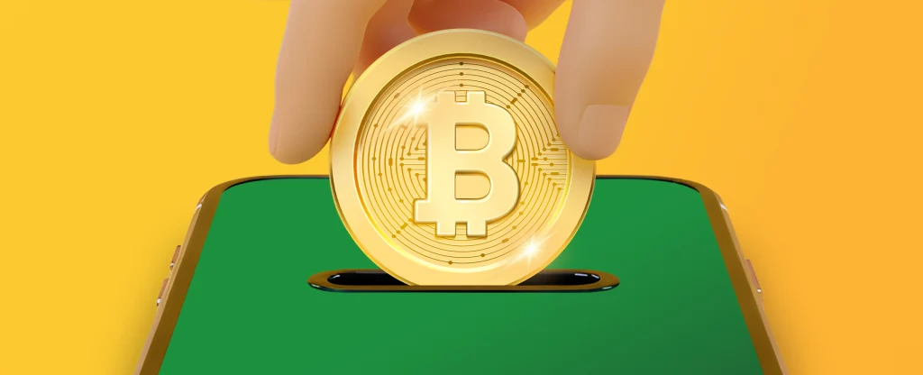 A golden Bitcoin coin being inserted into a slot on a smartphone screen, symbolising cryptocurrency payments or deposits, on a bright yellow background.