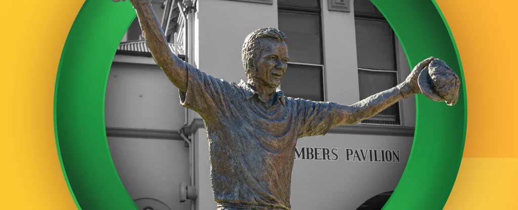 Bronze statue of Australian cricketer Steve Waugh with arms raised and cap in hand, standing in front of the Members Pavilion at the Sydney Cricket Ground, framed by a green circle on a bright yellow background.